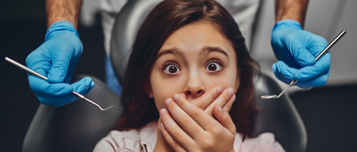 girl afraid of the dentist and clasping her hands over mouth