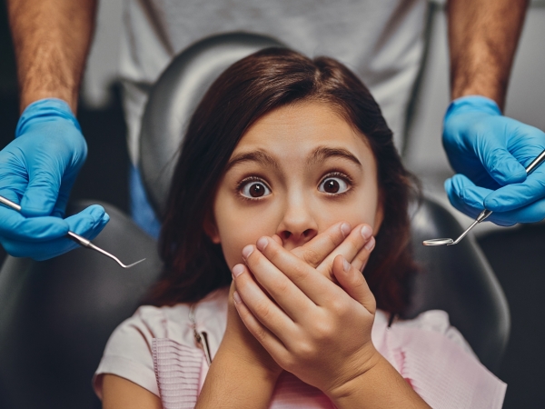 girl afraid of the dentist and clasping her hands over mouth